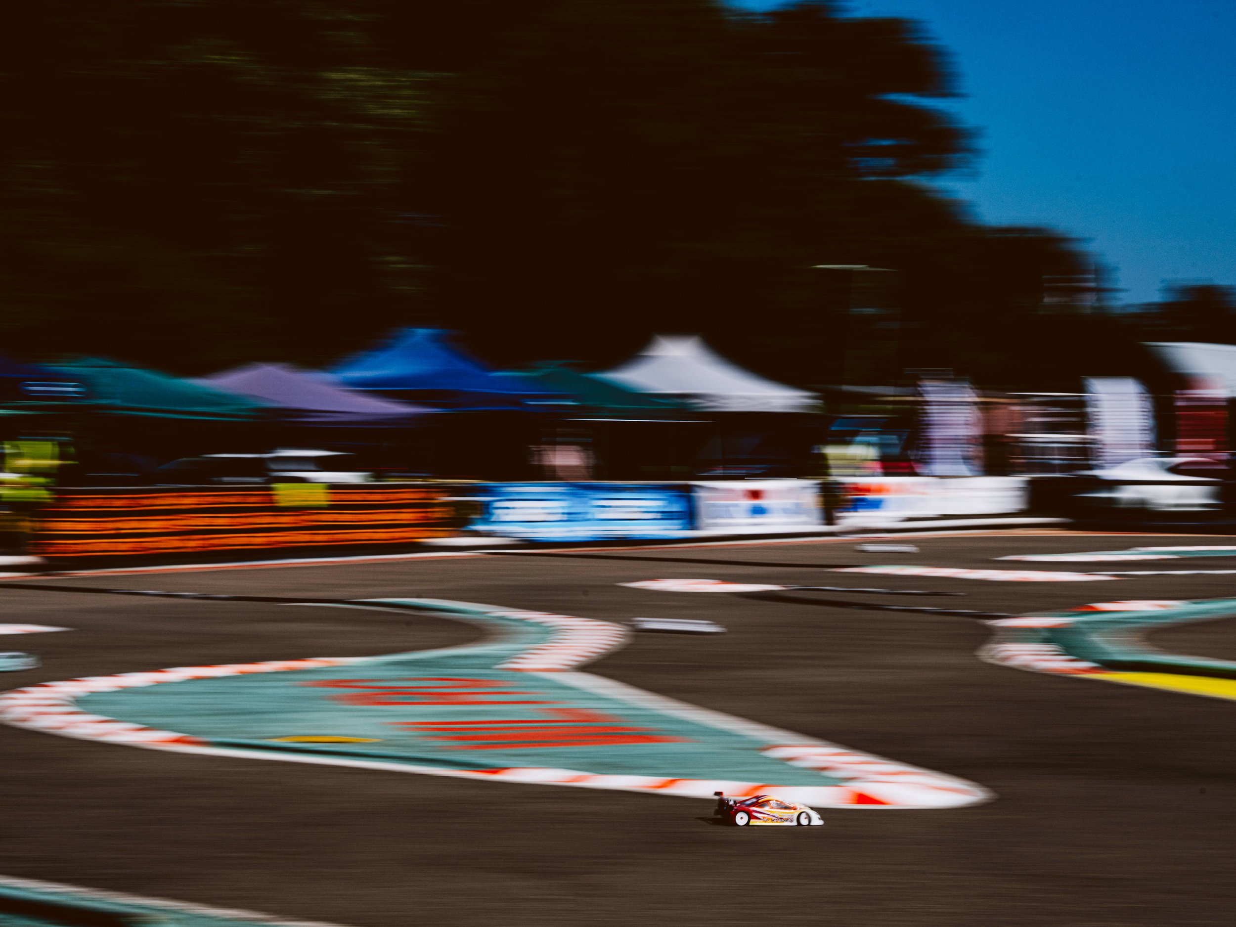 Motion-blurred RC touring car racing through a corner at an outdoor club circuit